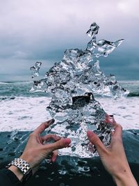 Cropped hands of man holding ice at beach against sky