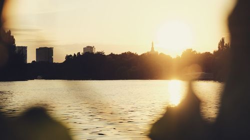 Silhouette buildings by river against sky during sunset