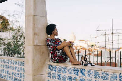 Contemplative woman with sandal sitting on wall