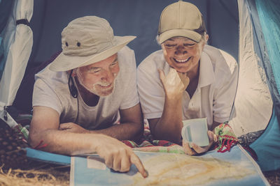 Smiling couple reading map in tent at forest
