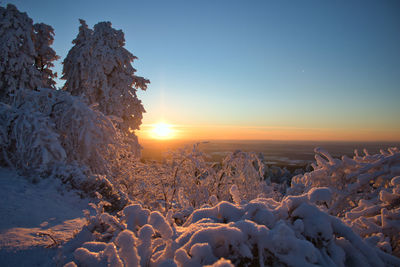 Snow covered landscape against sky during sunset