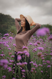 Side view of young woman wearing hat standing amidst plants