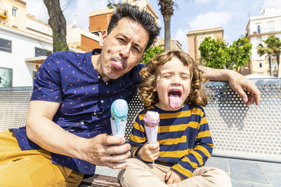 Spain, barcelona, happy father and son sitting on bench enjoying an ice cream