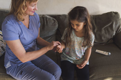 High angle view of doctor checking pulse of girl while sitting on sofa at home