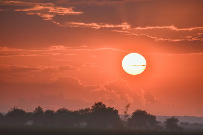 Orange sunset in nature. sun between the clouds, and foggy ground and trees.