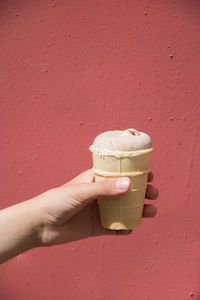 Cropped hand holding ice cream cone against wall