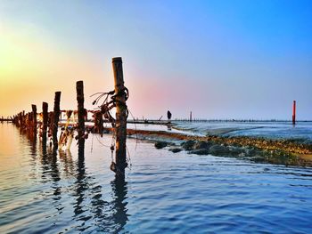 Wooden posts on beach against sky during sunset