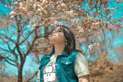 Close-up of young woman standing against tree