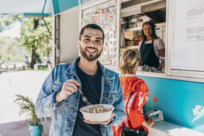 Portrait of smiling young man eating fresh tex-mex in bowl against food truck