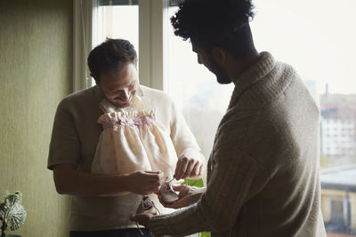 Smiling homosexual couple holding baby clothes