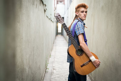 Portrait of man holding guitar against wall