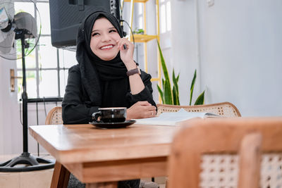 Young woman using mobile phone while sitting on table