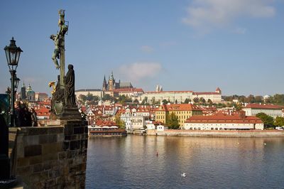 Statue of buildings by river against sky in city