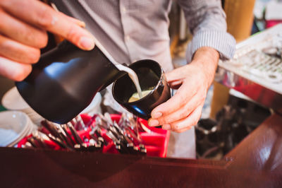 Midsection of barista pouring coffee in cup from container at cafe