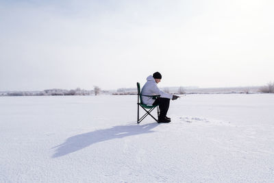 Full length of man sitting on snowy field