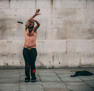 Full length of shirtless man standing against wall