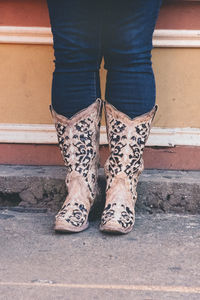 Low section of woman wearing cowboy boots standing against wall