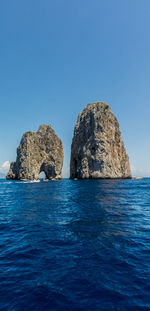 Rock formation in sea against clear blue sky