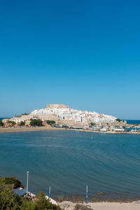 Buildings by sea against clear blue sky