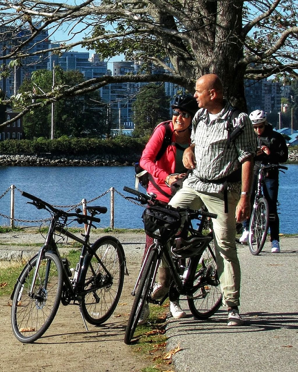bicycle, transportation, cycling, two people, full length, men, tree, adult, leisure activity, nature, togetherness, lifestyles, casual clothing, mode of transportation, day, mountain bike, women, vehicle, plant, city, sports equipment, activity, sports, land vehicle, young adult, architecture, road cycling, friendship, smiling, endurance sports, sunlight, outdoors, female, emotion, happiness, bonding, water, mature adult, built structure, cycle sport, riding, standing