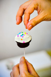 Hand putting colourful sprinkles on a cake pop.