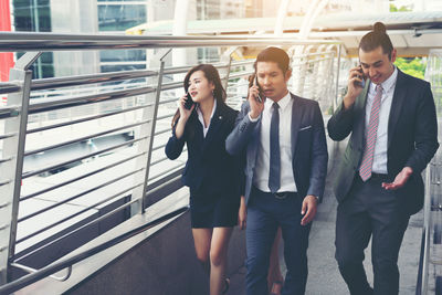 Colleagues using phones while walking on elevated walkway 