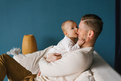 Smiling caucasian dad holds his loving son in his arms and hugs his chest. the child bites dad's 