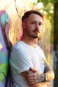 Portrait of young man standing against graffiti wall