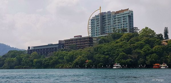 View of buildings by river against cloudy sky