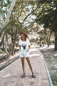 Portrait of young woman standing on footpath amidst trees