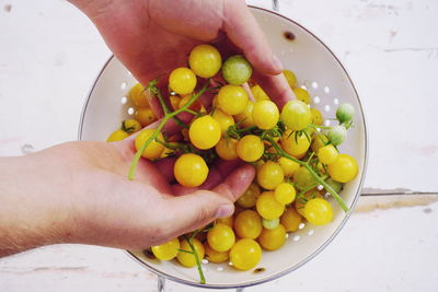 Cropped hands holding yellow fruits in bowl