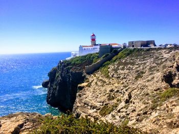 Lighthouse on mountain by sea against clear sky