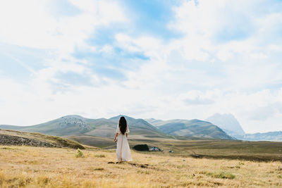 Rear view of woman standing on field against sky and mountain in abruzzo italy 