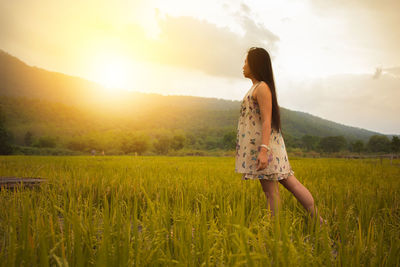 Woman standing on field against sky during sunset