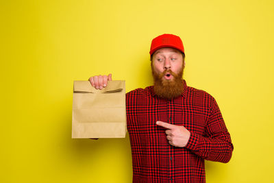 Portrait of man holding hat against yellow background
