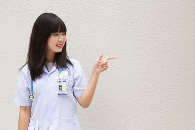 Young female doctor standing against wall