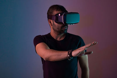 Young man in vr glasses headset interact with virtual reality in color neon light, future technology