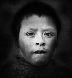 Close-up portrait of boy with freckles on face against black background