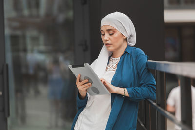 Young woman in hijab using digital tablet standing outdoors