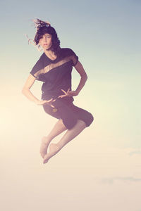 Low section of woman jumping against sky during sunset