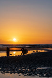 Silhouette groynes on beach against sky during sunrise