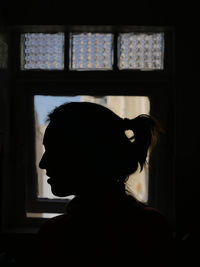 Portrait of silhouette woman standing against window at home