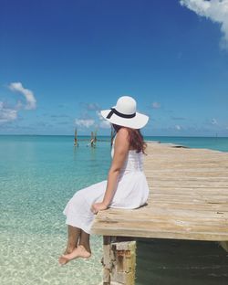 Side view of woman sitting on pier over sea against blue sky