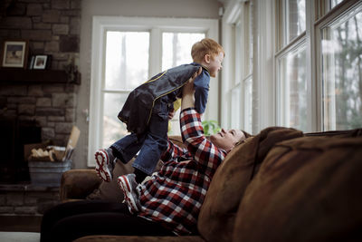 Happy mother picking up son while sitting on sofa at home