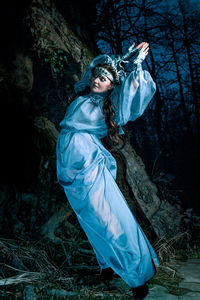 A gloomy full length portrait of a woman in makeup and a night witch costume on a dark background