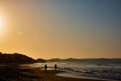 Silhouette people on beach against clear sky during sunrise