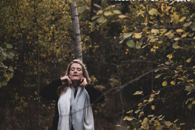 Mid adult woman with closed eyes standing against trees in forest