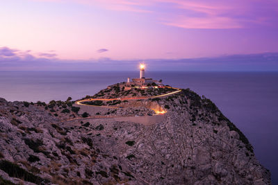 Scenic view of sea by illuminated buildings against sky during sunset