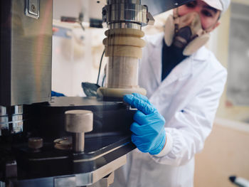 Male worker in protective uniform operating capsule filling machine at pharmaceutical manufacturing plant