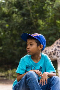 Boy looking away while sitting against blue wall